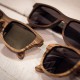 Tres parells d'ulleres de sol amb muntura de fusta i lents fosques es col·loquen sobre una superfície de fusta de color clar. Les ulleres de sol estan disposades en diferents angles, destacant els seus patrons únics de veta de fusta.